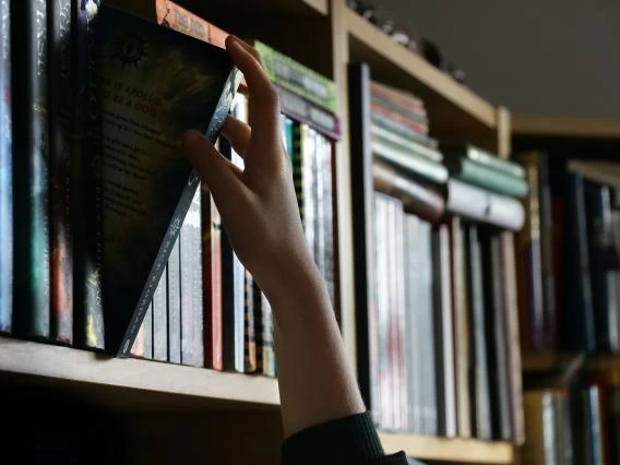 hand reaching for a book pulling it from a bookcase